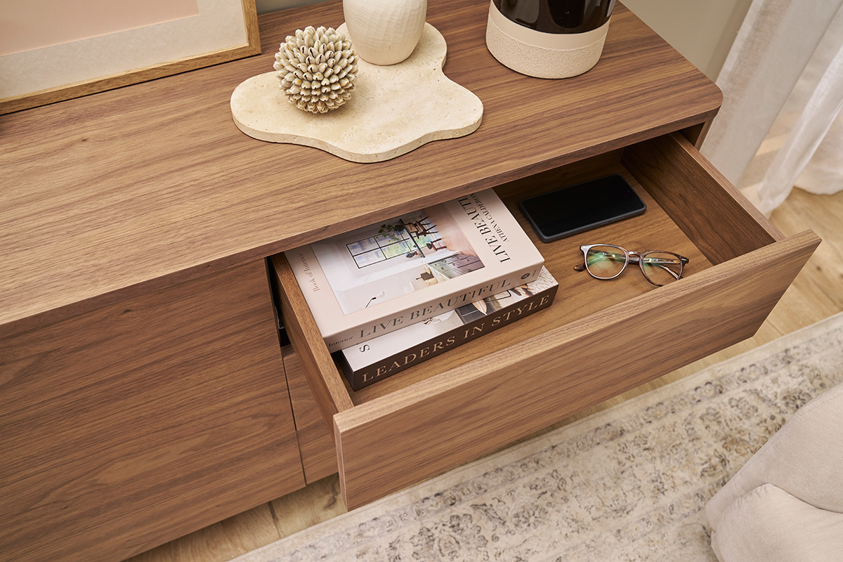 Buffet de madera oscura con cajn abierto, libros y gafas ordenados en su interior.