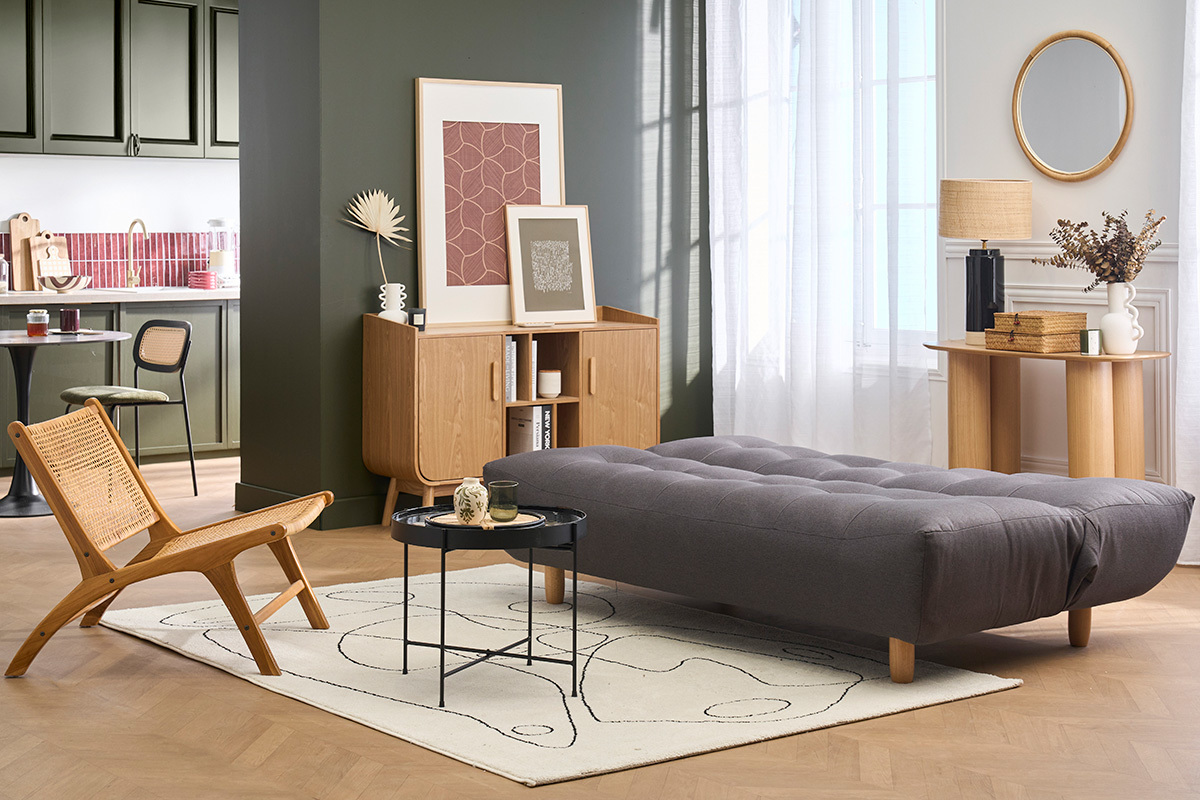Sof� convertible gris oscuro de 3 plazas, patas de madera clara, dispuesto en un sal�n moderno.