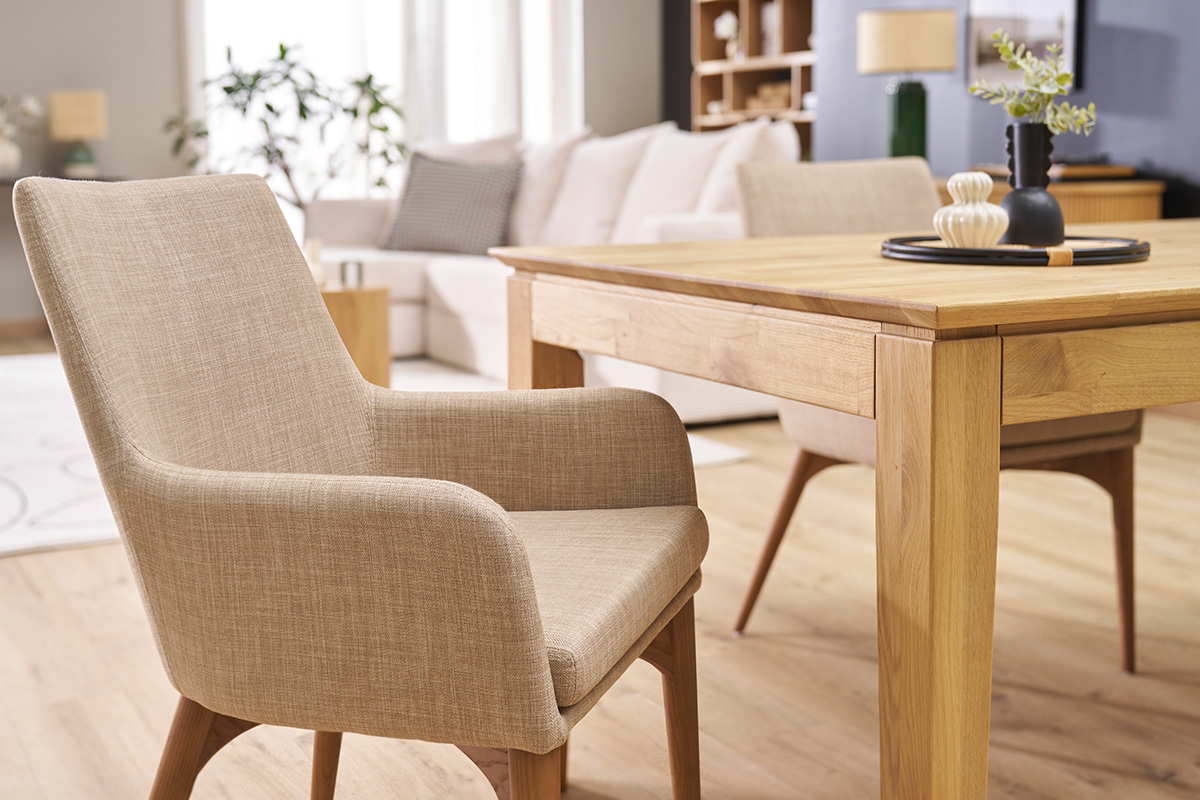 Silla de tela beige con brazos alrededor de una mesa de madera, vista en �ngulo en un interior.