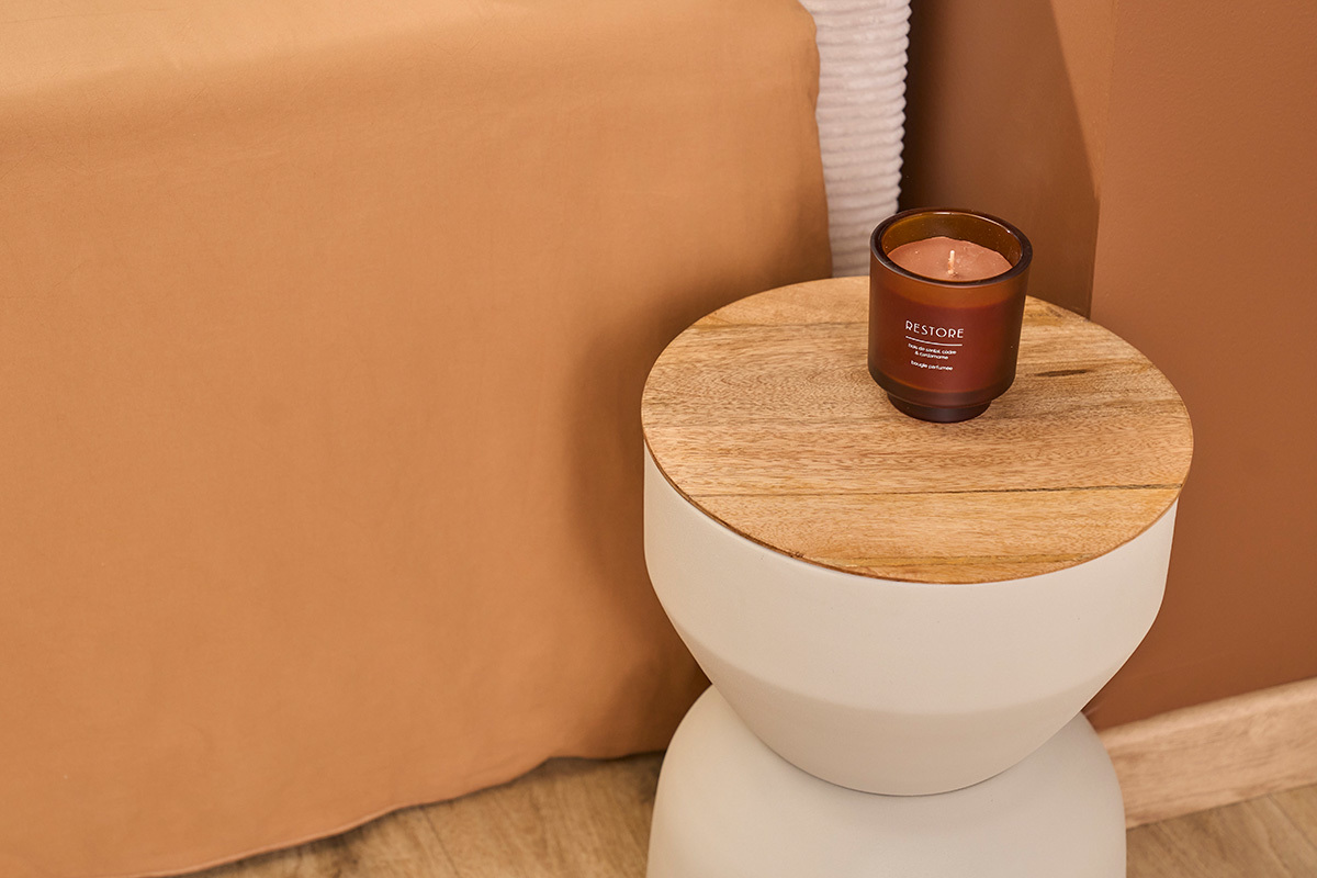 Mesa auxiliar redonda de metal beige y tapa de madera con vela, vista desde arriba.