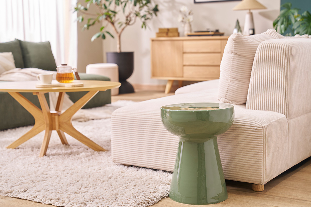 Mesa auxiliar redonda de metal esmaltado en verde caqui al lado de un sof� beige, vista ampliada.