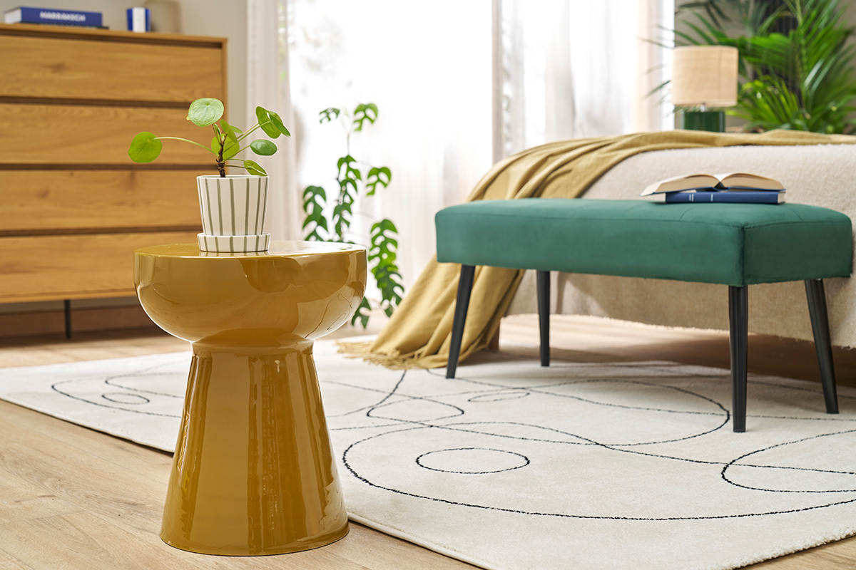 Mesa auxiliar redonda de metal esmaltado en bronce con planta vista de frente en una habitaci�n.