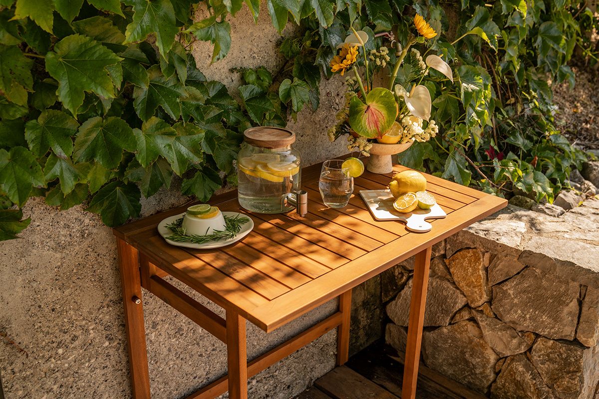 Mesa de balc�n plegable de madera maciza con decoraciones, vista desde arriba, rodeada de plantas.
