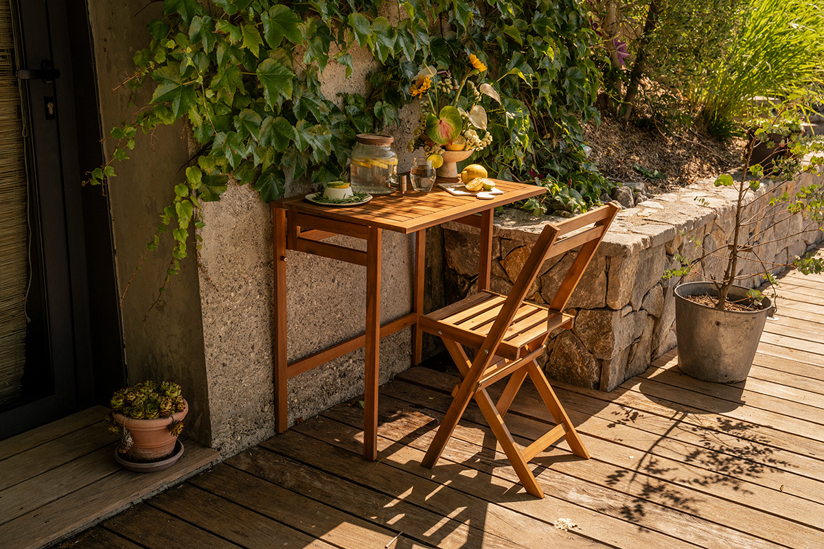 Mesa de balc�n plegable de madera maciza L80 cm, vista de 3/4 con silla y decoraciones en un balc�n