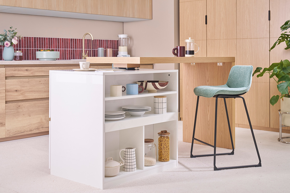 Isla de bar modular blanca y de madera de roble con estanter�as, taburete verde, cocina al fondo.