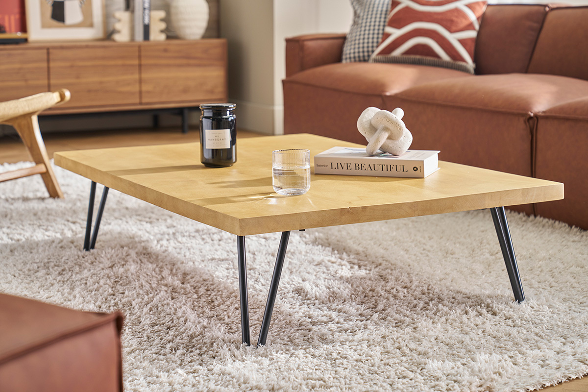 Mesa baja rectangular de madera de mango sobre alfombra, vista lateral con objetos decorativos.