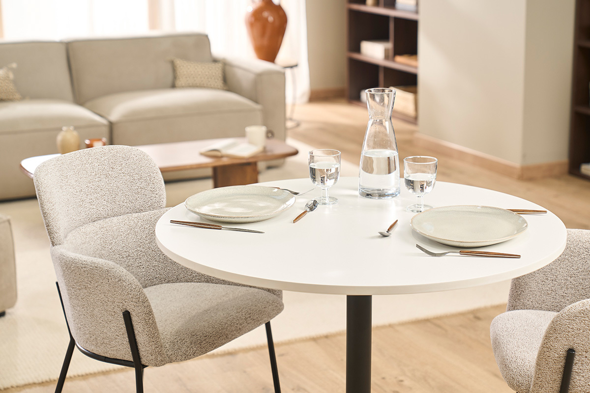 Mesa de comedor redonda blanca y metal negro CALISTA con vajilla y jarra, vista superior.