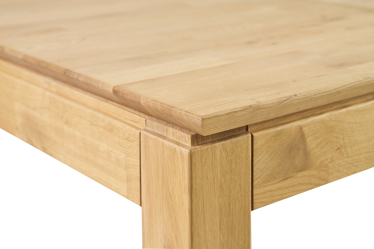 Detalle de la esquina de una mesa de comedor de madera clara, visible la tapa y la pata.