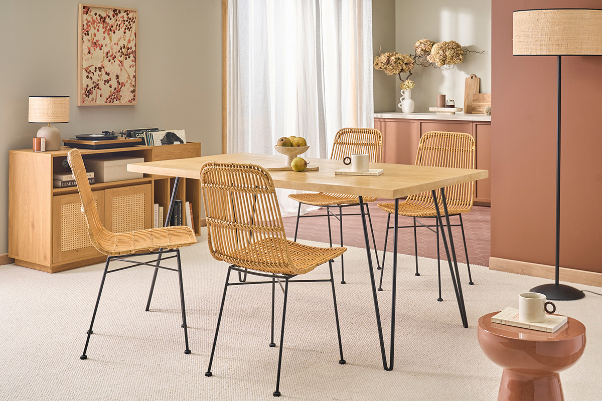 Mesa de comedor de madera con patas de metal negro, rodeada de sillas de rat�n, vista de tres cuartos.