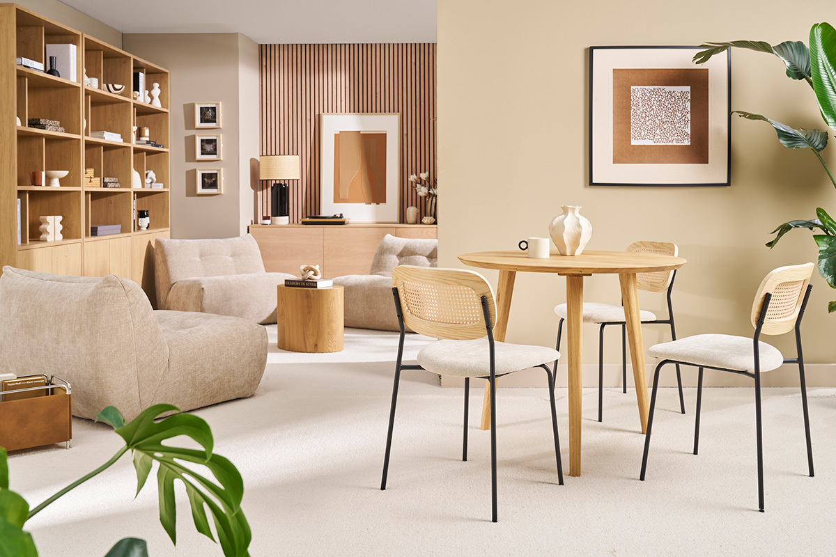 Mesa de comedor redonda de madera clara con cuatro sillas, vista general de una sala de estar moderna.