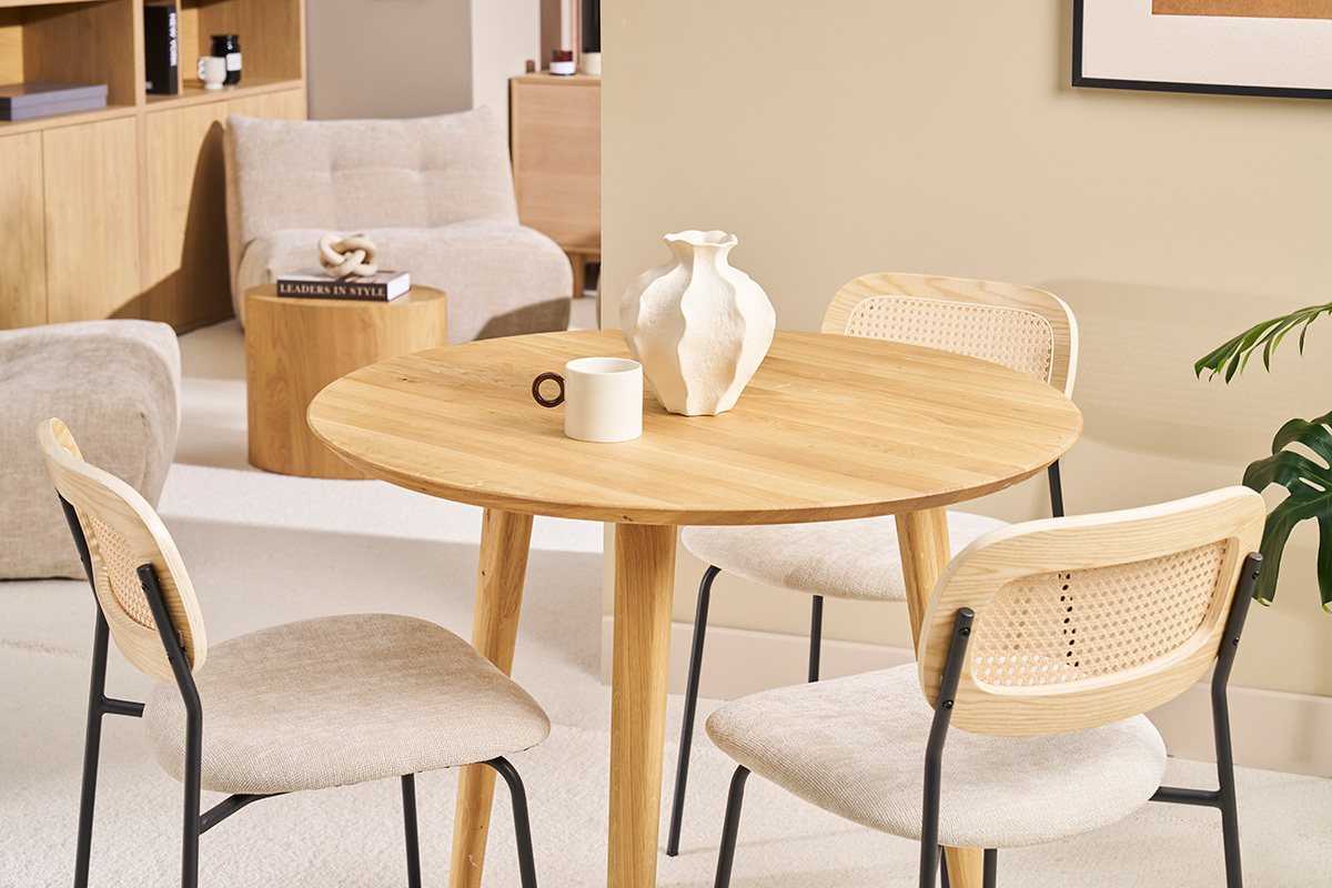 Mesa redonda de madera clara con sillas, vista general del comedor.