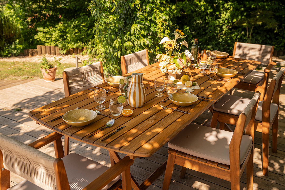 Mesa de jard�n extensible de madera maciza, vista superior con platos y vasos listos para una comida.
