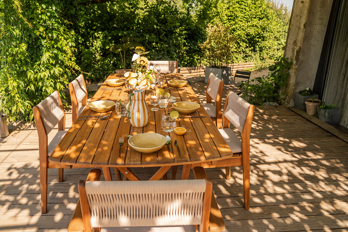 Mesa de jard�n extensible de madera maciza, vista lateral con vajilla, lista para una comida al aire libre.
