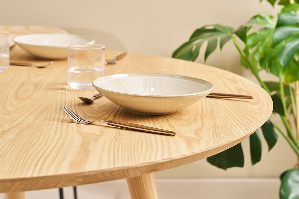 Mesa redonda de roble slido con cubiertos y plato, vista cercana.