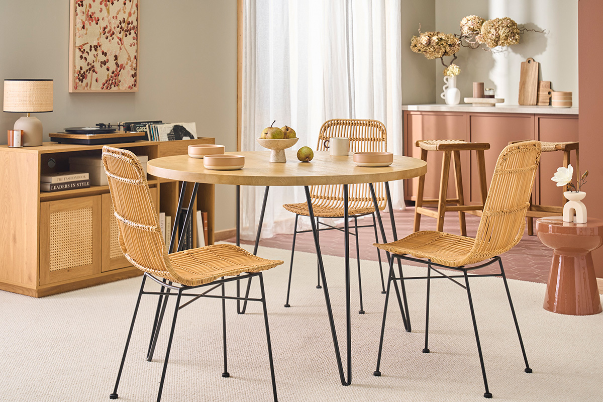 Mesa redonda de madera con patas de metal, rodeada de sillas de mimbre, en un interior moderno.