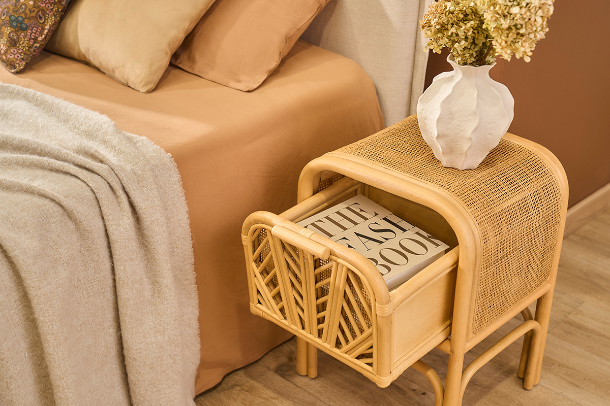 Mesa de noche de rat�n GALON con caj�n abierto que contiene un libro, vista en �ngulo.