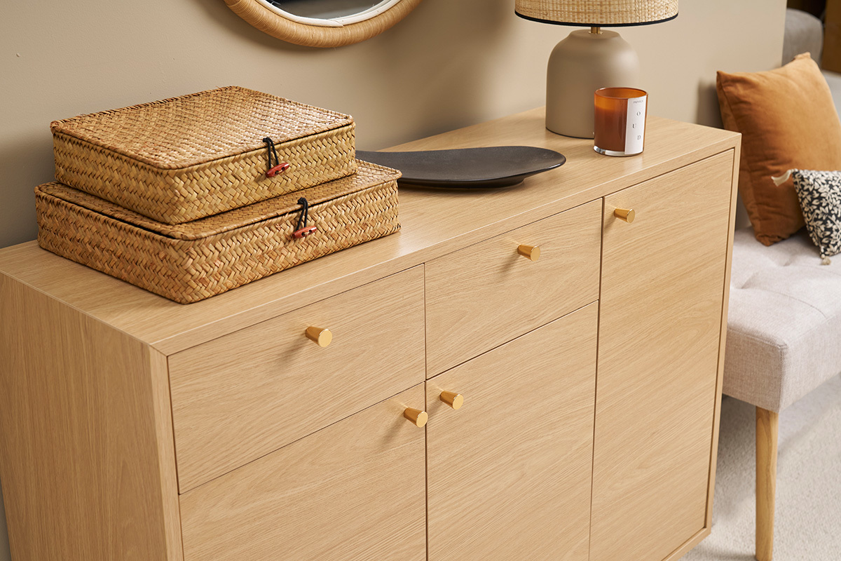 Mueble de entrada de madera clara con manijas doradas, dos canastas de mimbre y decoraciones en la parte superior.