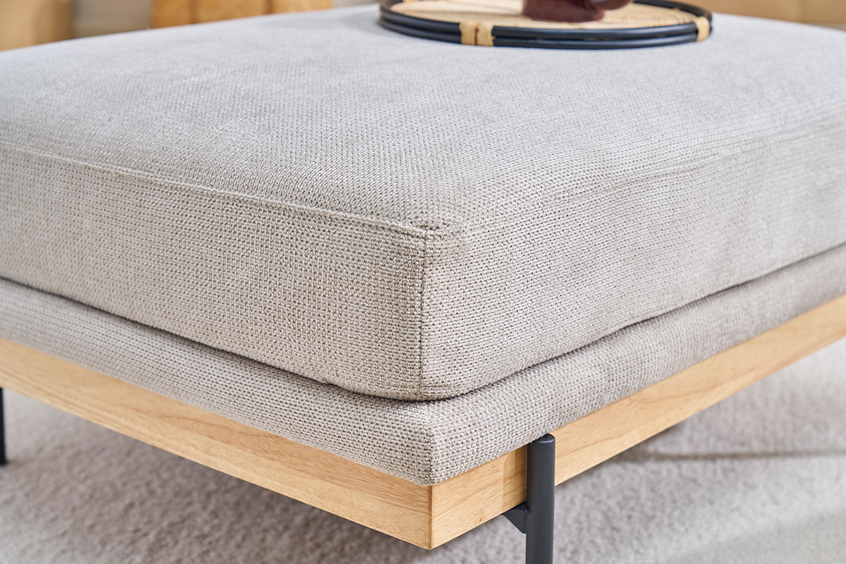 Puf TODD en tela de chenilla beige, vista de cerca, con base de madera y patas de metal negro.
