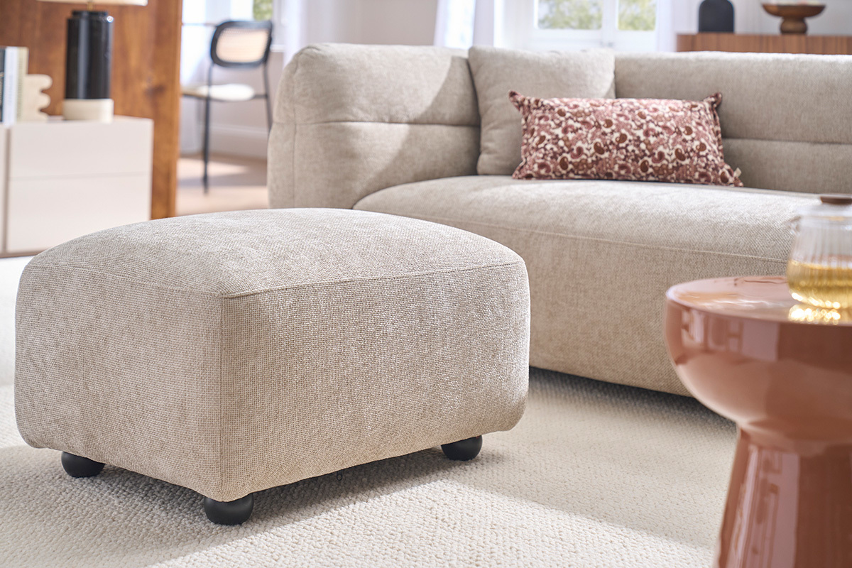 Puf reposapi�s de tela beige, vista lateral, en un sal�n moderno.