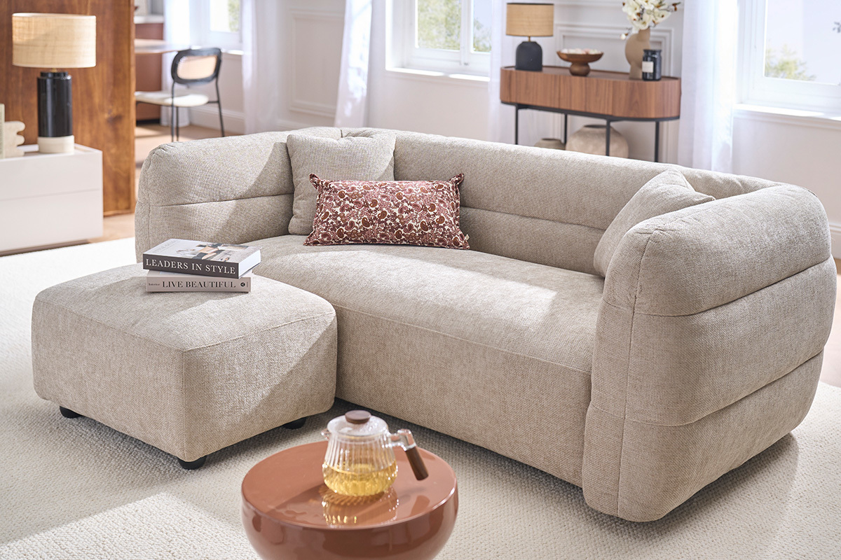 Puf reposapi�s de tela beige JOYA, junto a un sof�, vista general en un interior luminoso.