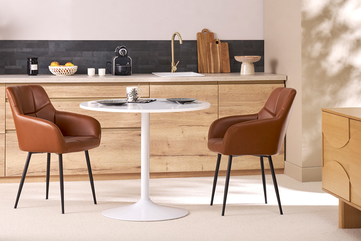 Sillas acolchadas marrones y metal negro MONTERO alrededor de una mesa blanca.