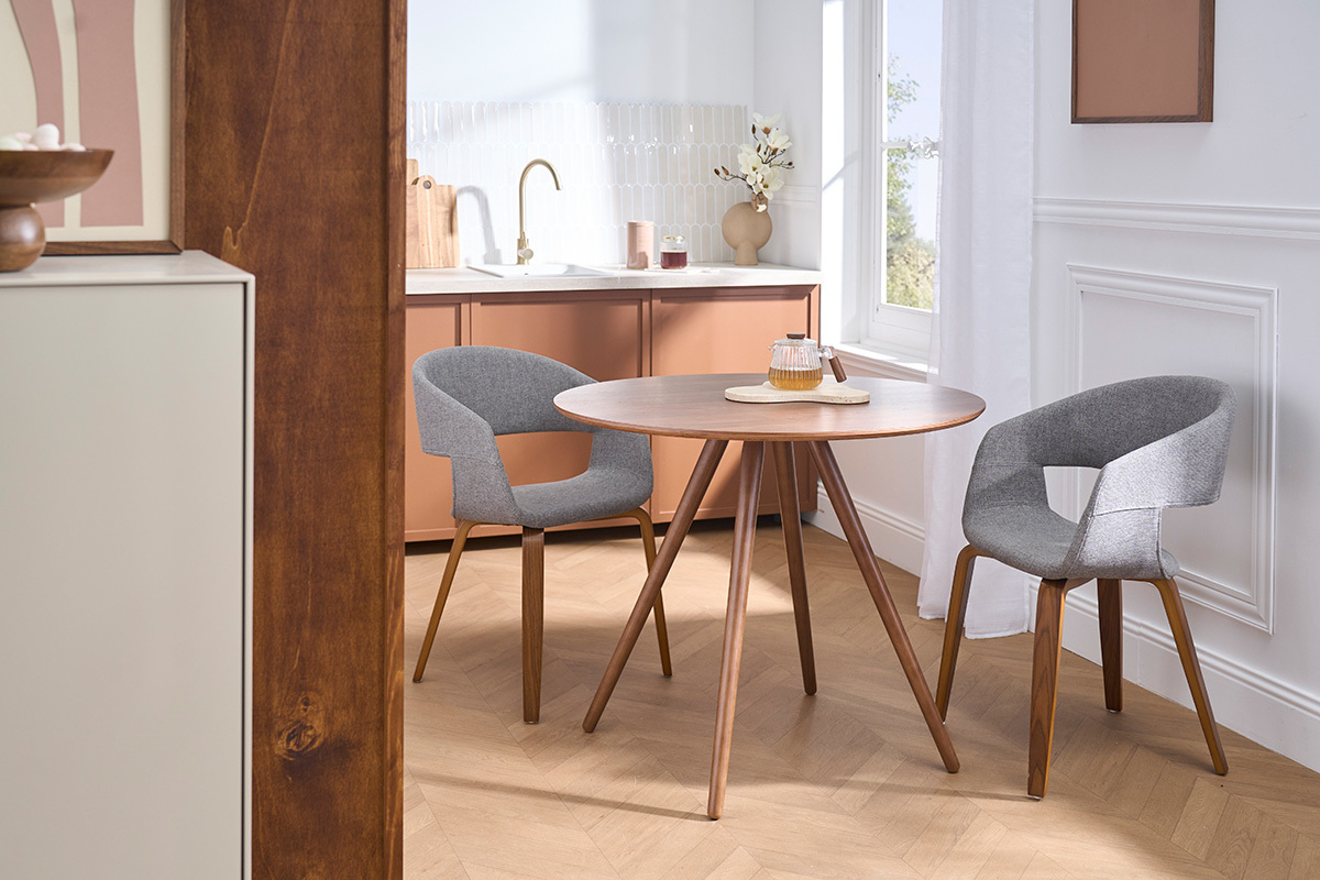 Sillas de dise�o grises de tela con patas de madera oscura alrededor de una mesa redonda en un interior moderno.