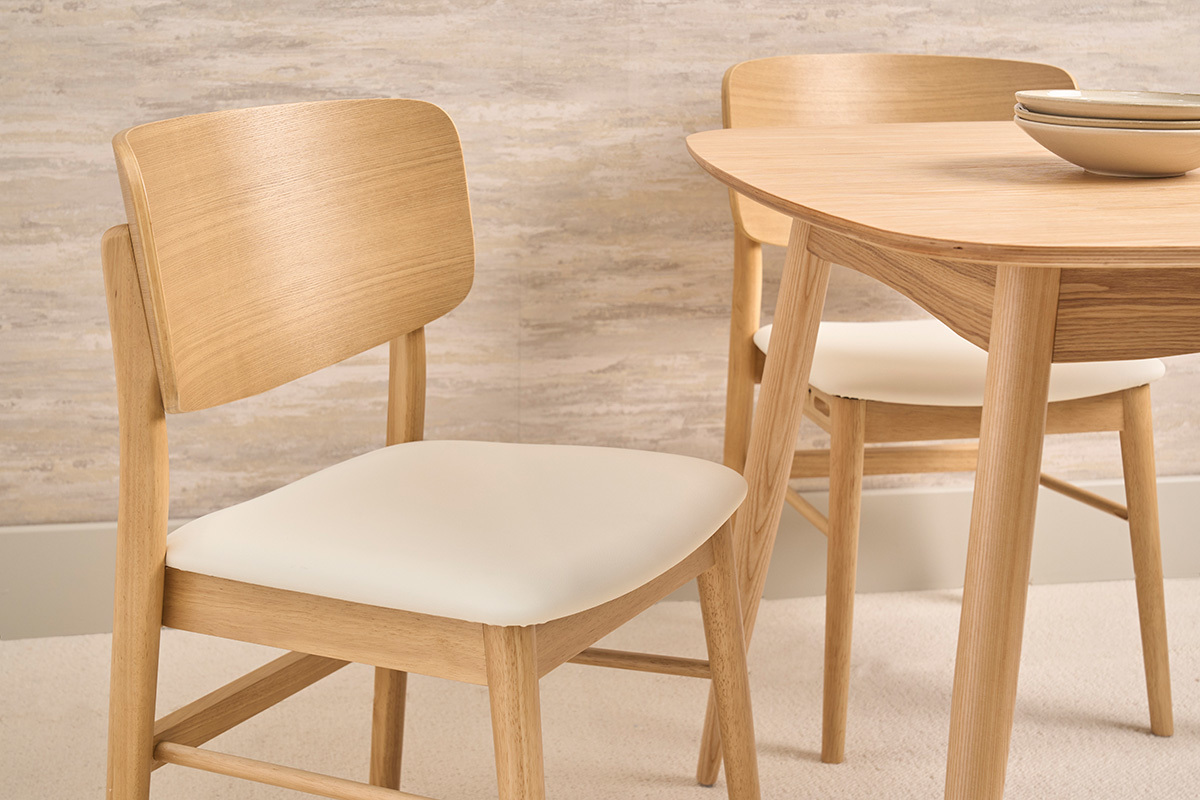 Sillas escandinavas blancas y de madera clara, vista de cerca, con una mesa de madera al fondo.