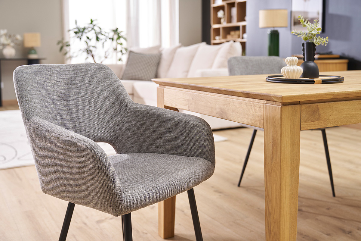 Silla de tela efecto terciopelo gris con patas de metal negro, vista 3/4 cerca de una mesa de madera.
