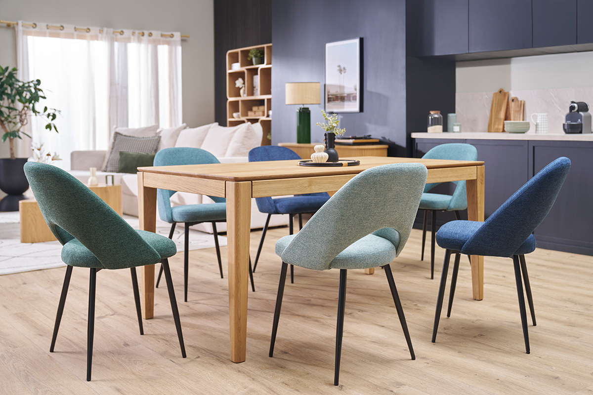 Sillas verde celadn en tela de terciopelo y patas metlicas negras alrededor de una mesa de madera, vista interior.