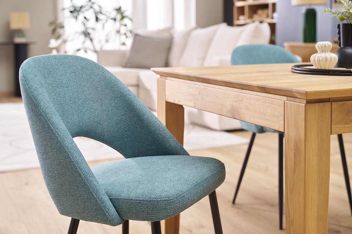 Sillas vintage verde grisceo con patas de metal negro, al lado de una mesa de madera.