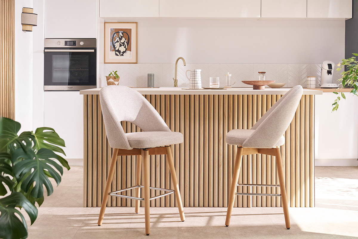 Taburetes de bar beige de tela con patas de madera maciza de caucho frente a una encimera de cocina.