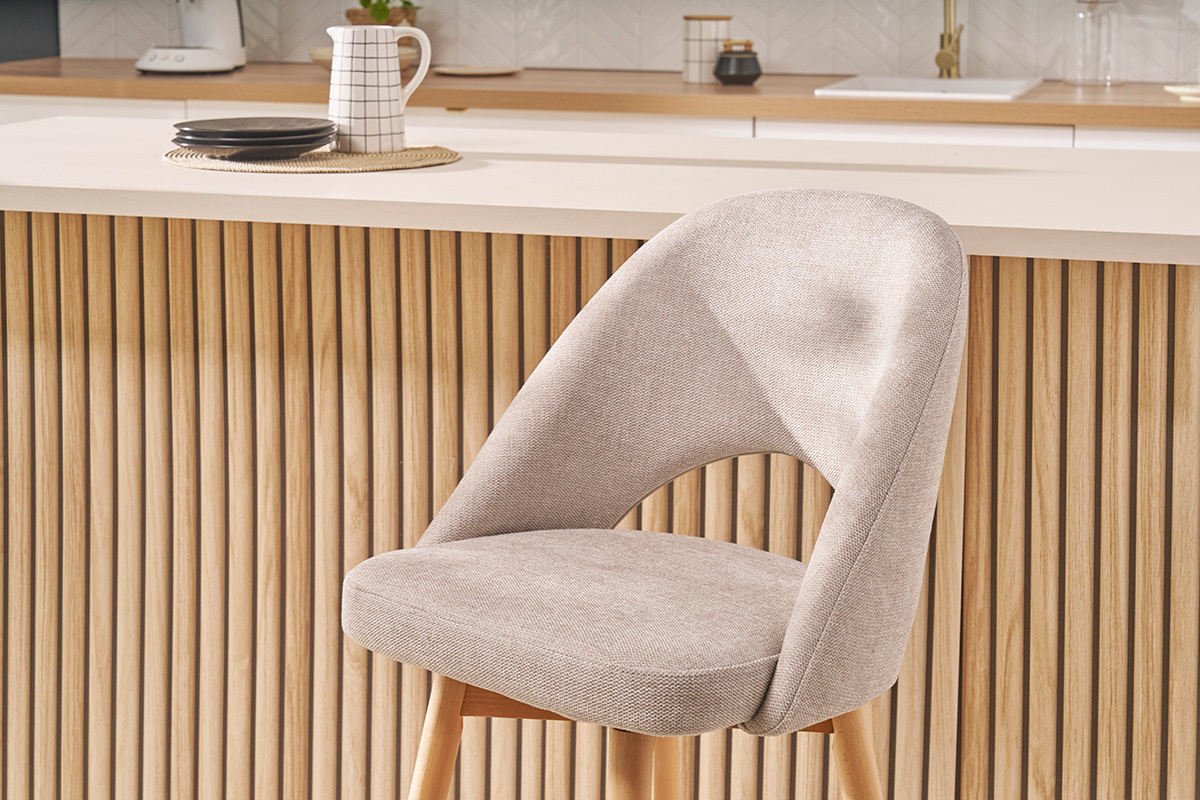 Taburete de bar escandinavo de tela beige y madera maciza de caucho frente a un mostrador de madera.