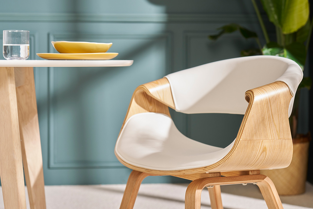 Chaise de dise�o ARAMIS blanca y madera clara, vista de perfil, con mesa y plato en el fondo.