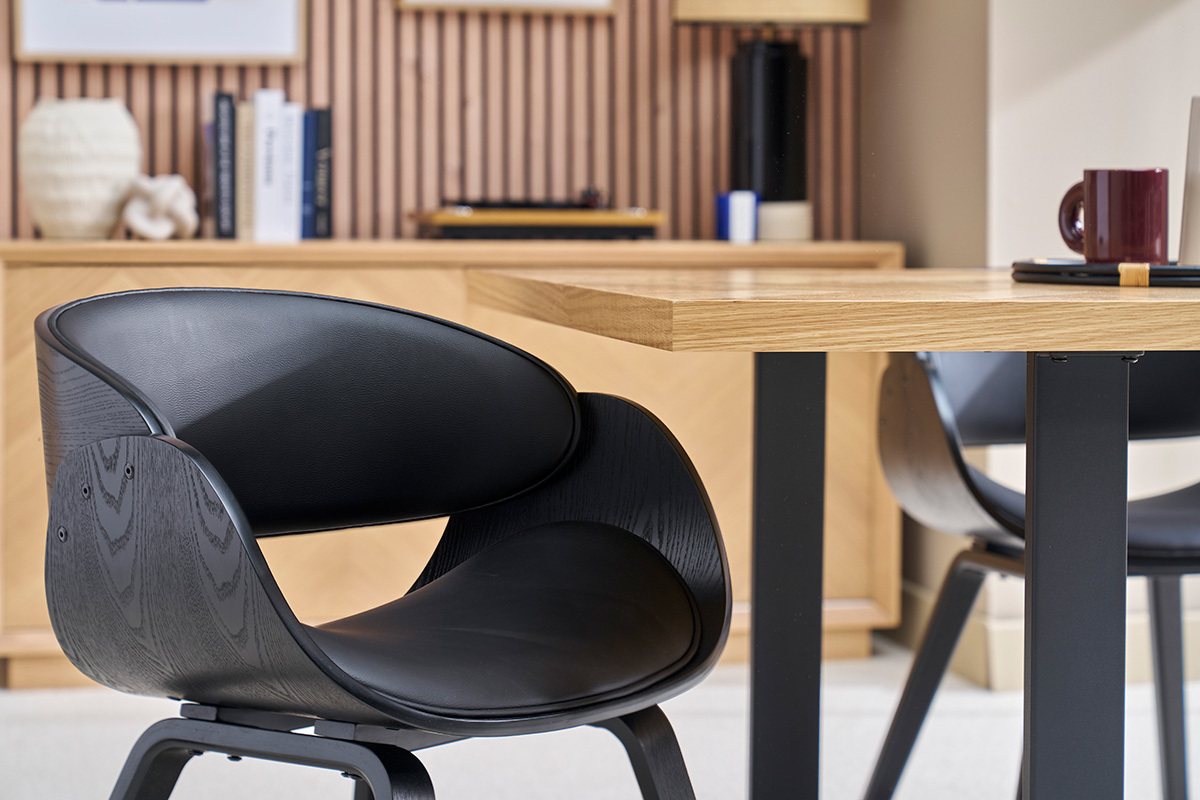 Silla de diseo negro BENT con respaldo de madera, vista lateral al lado de una mesa de madera clara.