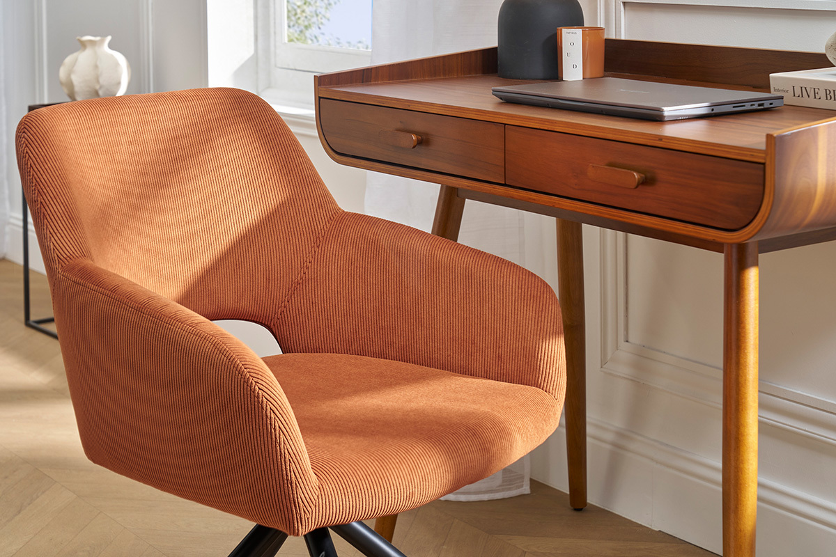 Silla giratoria de pana en color tierra quemada al lado de un escritorio de madera, vista interior.