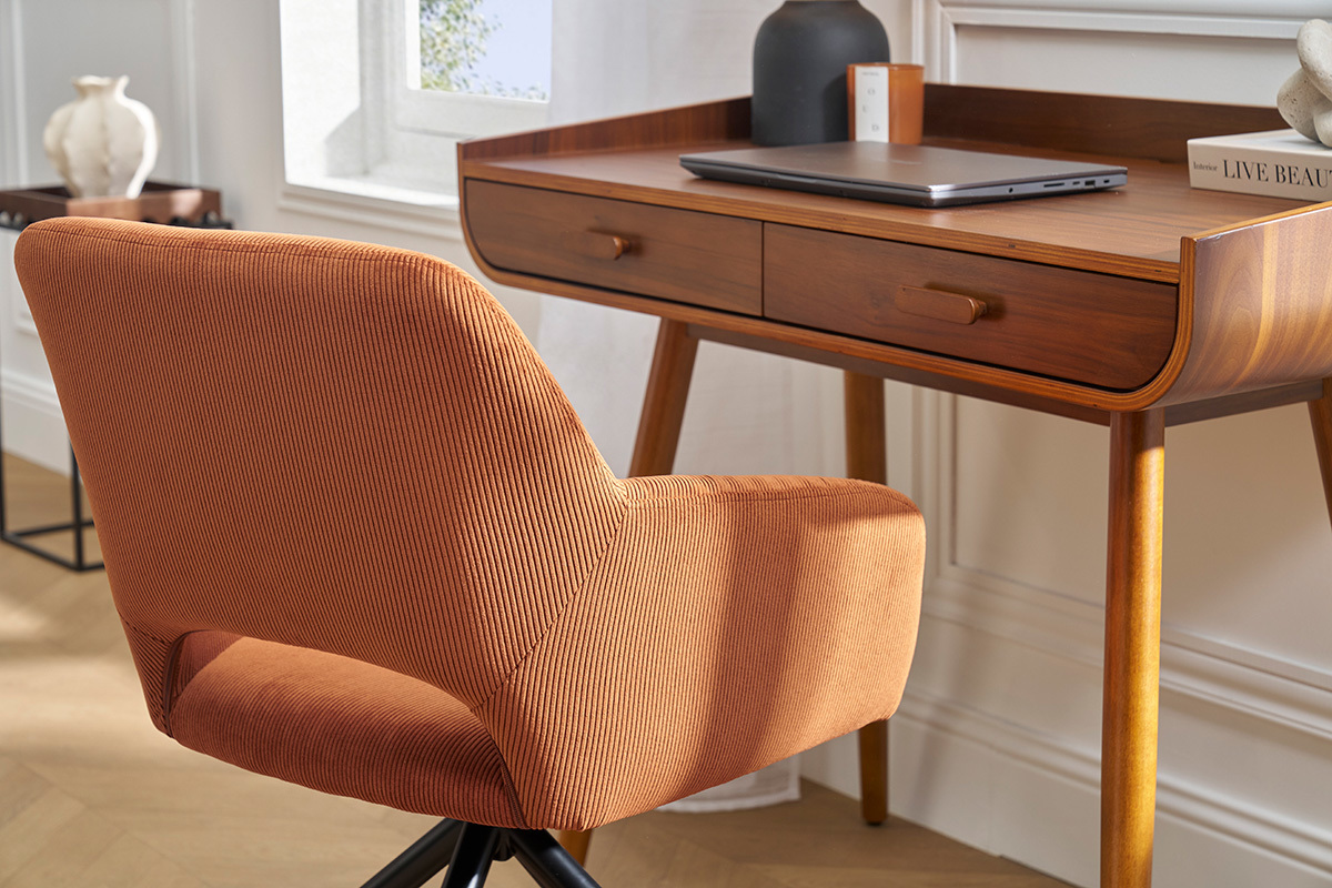 Silla giratoria de pana en color tierra quemada frente a un escritorio de madera, vista trasera.