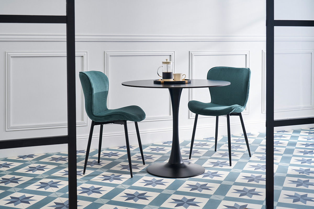 Dos sillas de pana azul pato con patas de metal negro alrededor de una mesa negra.
