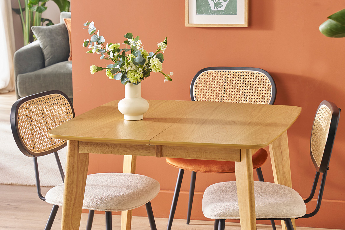 Dos sillas SWANN en tela blanca y rat�n alrededor de una mesa de madera clara, jarr�n con flores.