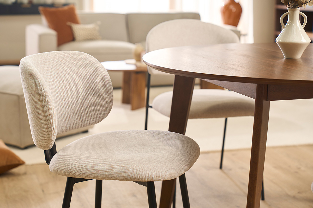 Sillas beige de tela con patas de metal negro alrededor de una mesa de madera, vista parcial.