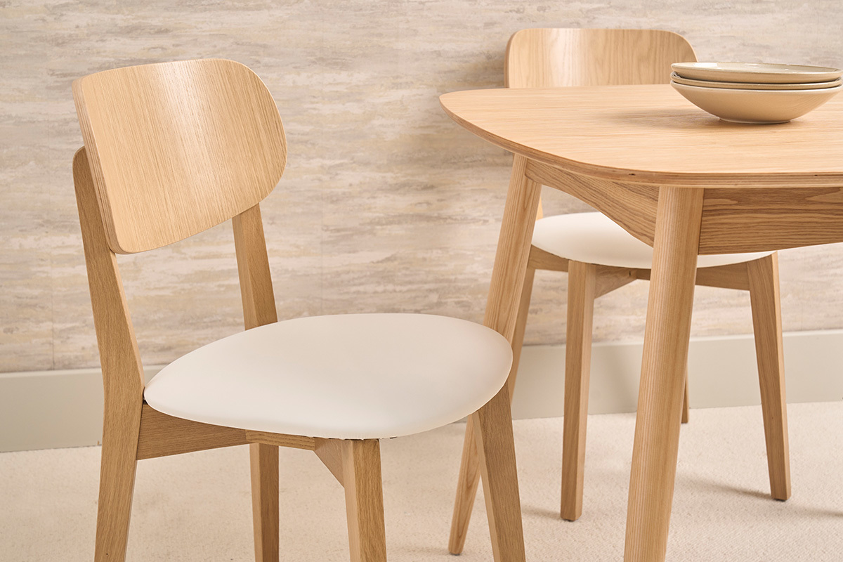 Sillas vintage de madera de roble claro y asiento blanco, vista en primer plano de dos sillas alrededor de una mesa.