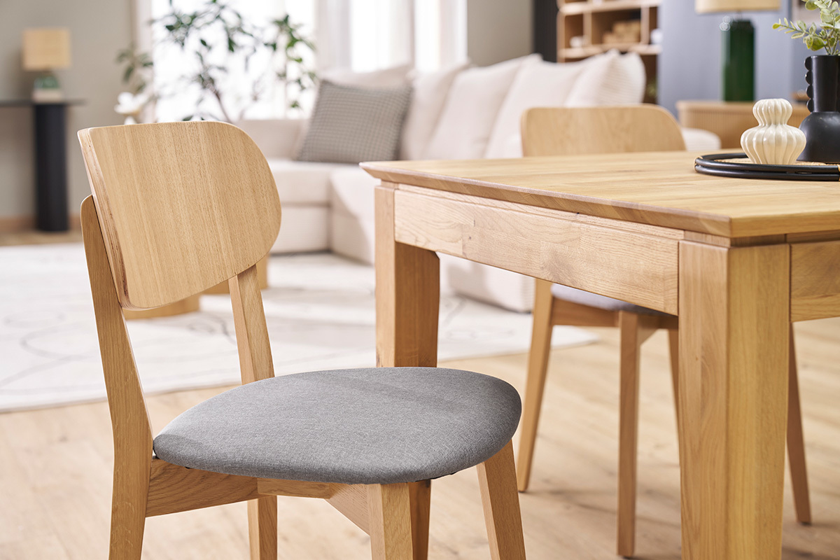 Silla vintage de madera clara con asiento de tela gris claro frente a una mesa de madera.