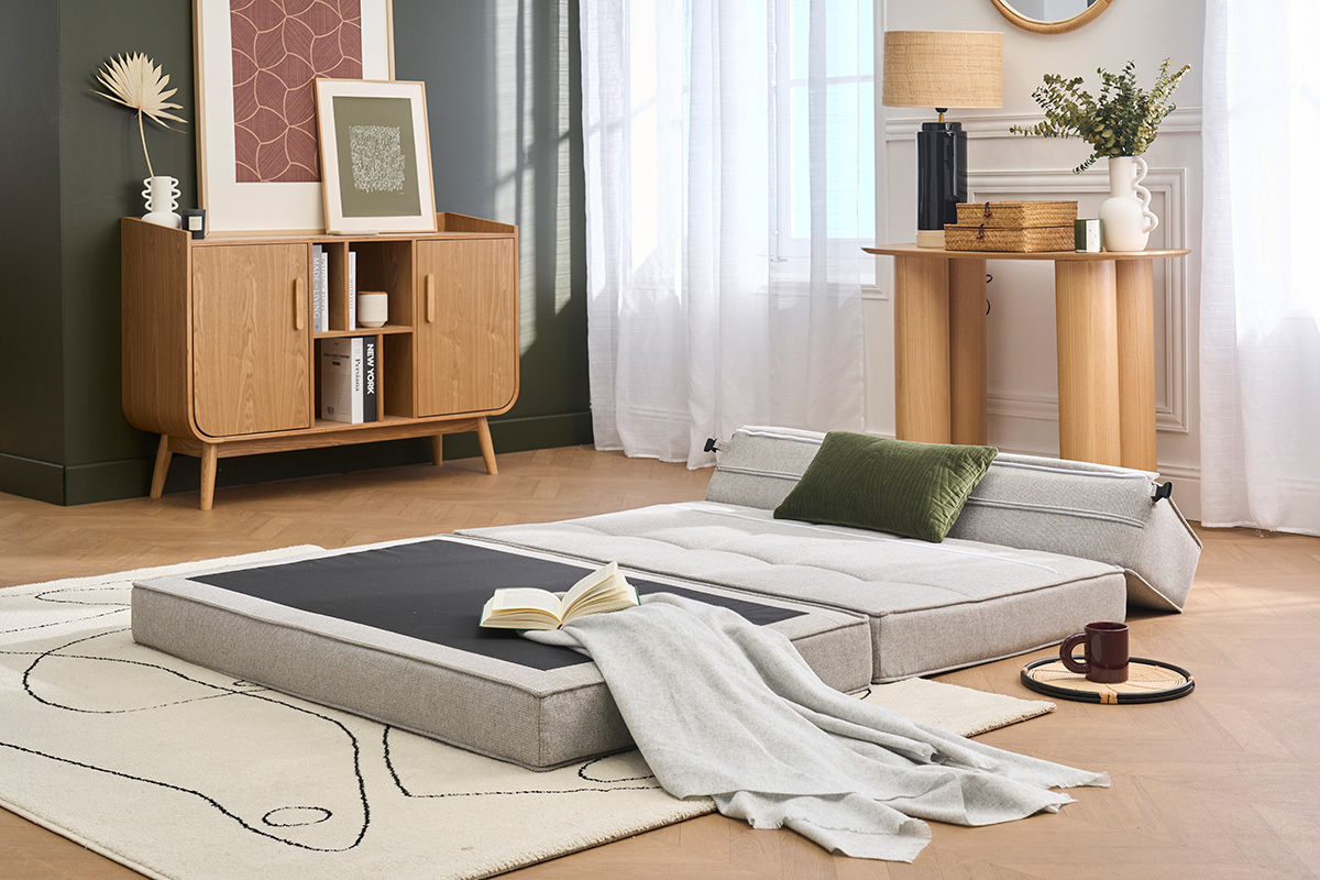 Sof� cama KATY de 2 plazas desplegado en cama, tela gris claro, coj�n verde, ubicado en un sal�n moderno.