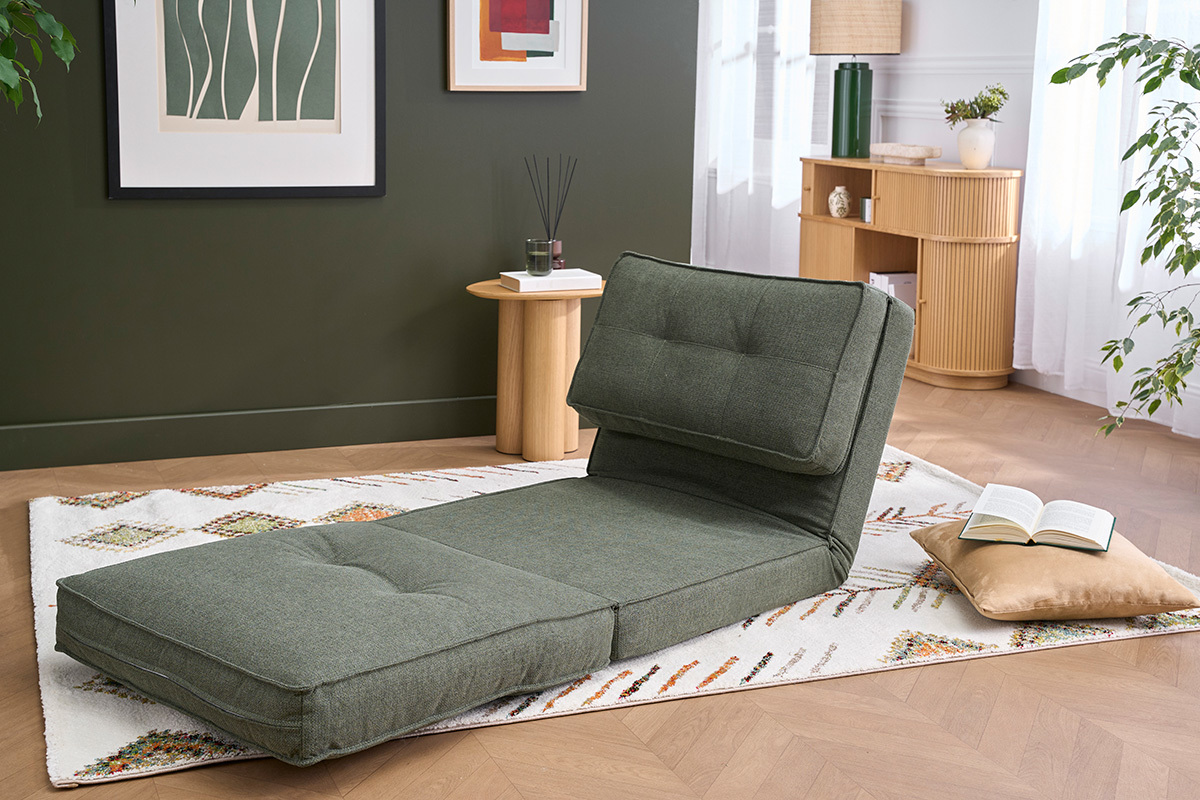 Sill�n convertible en tela verde caqui, vista lateral, sobre una alfombra en un sal�n luminoso.