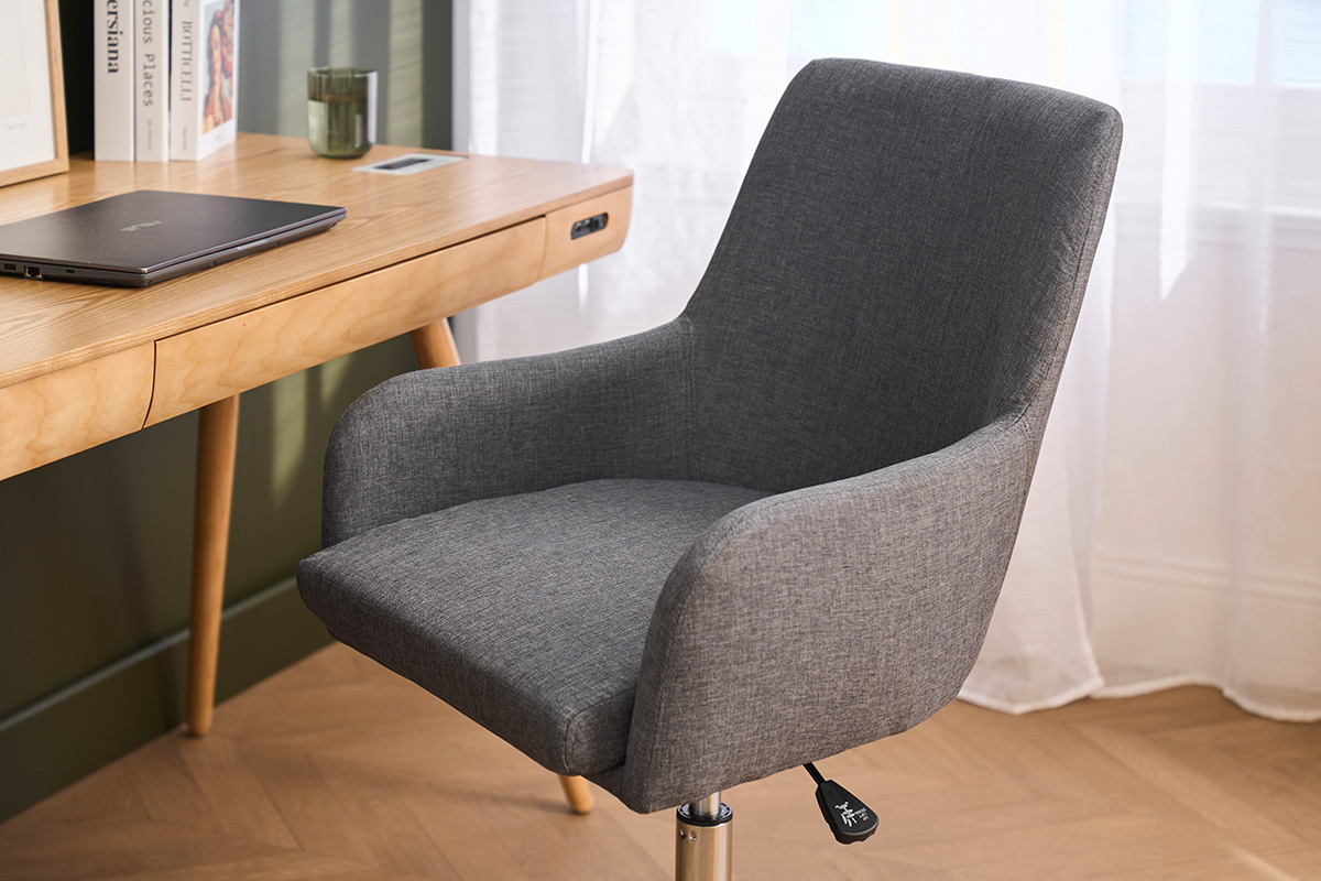 Silla de oficina de tela gris, vista de 3/4, con brazos delante de un escritorio de madera.