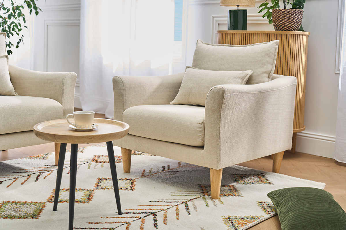 Butaca escandinava beige con cojines, mesa de centro, vista en tres cuartos.