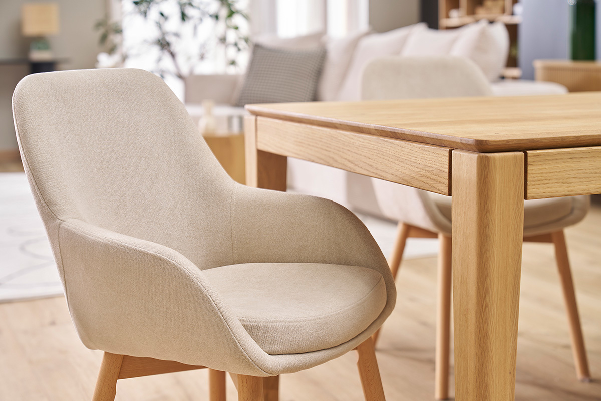 Sill�n escandinavo en tela beige y madera clara, vista lateral, al lado de una mesa de madera.