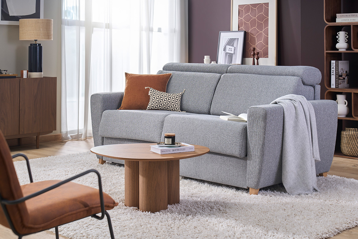 Sof� convertible de 3 plazas gris con reposacabezas ajustables, vista de 3/4 en un sal�n moderno