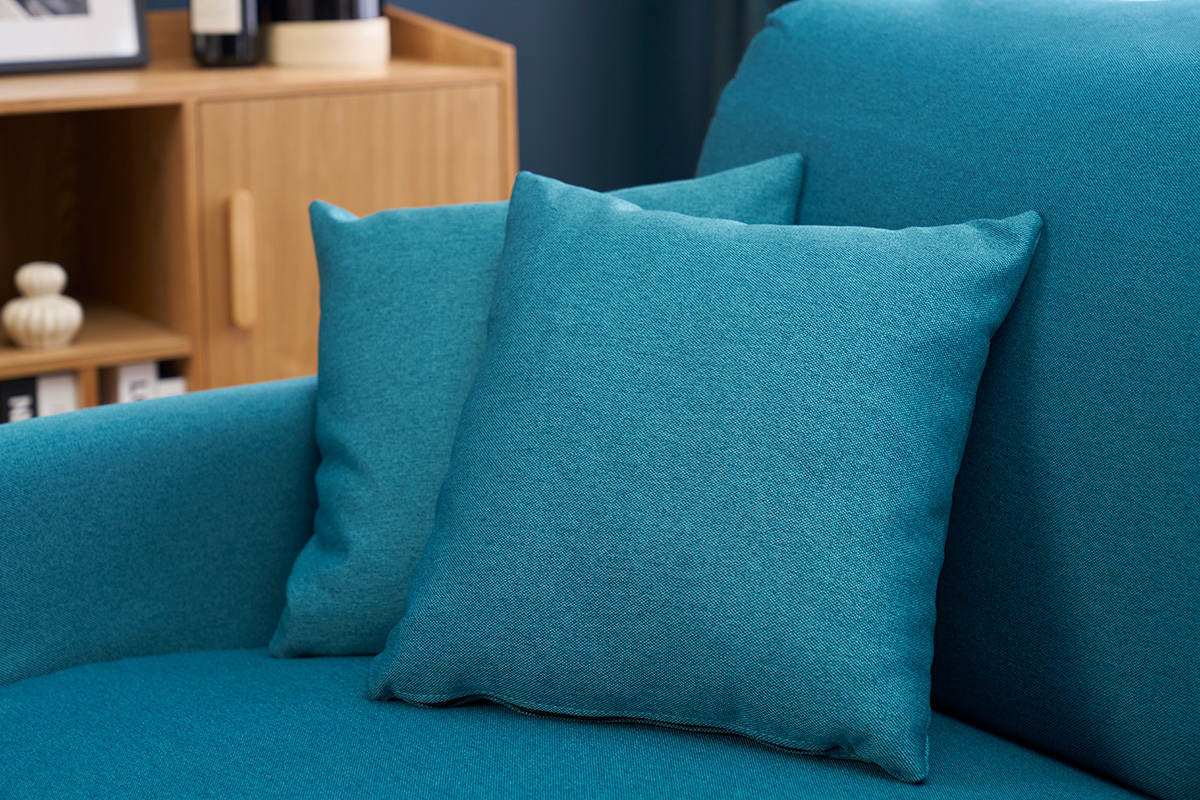 Cojines del sof cama azul petrleo SKANDY en vista cercana al lado de un mueble de madera.