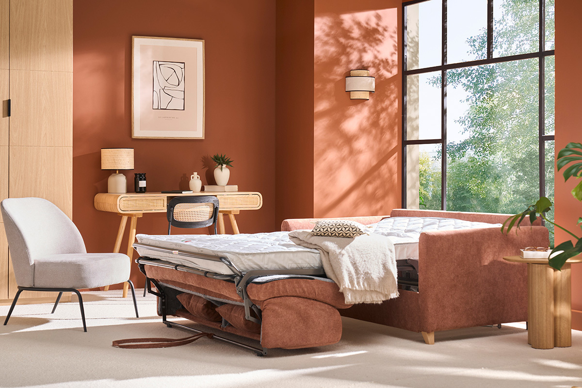 Sof convertible en tela terracota, colchn desplegado, en una sala con pared de color tierra cocida.