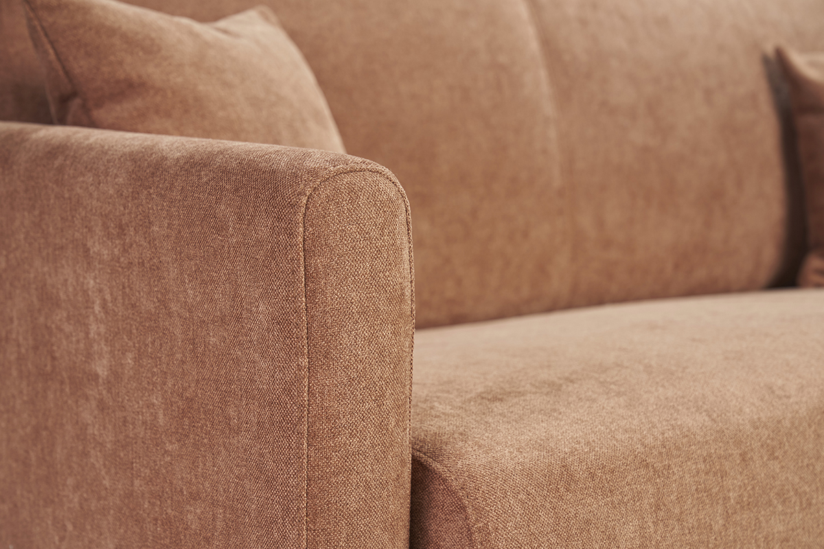 Detalle de un sof de tela efecto terciopelo en color tierra quemada, apoyabrazos visible.
